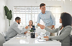 Diverse group of businesspeople having a meeting together at a table at work. Business professionals talking and planning in an office. Young caucasian businessman greeting a mixed race businesswoman with a handshake