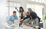 Happy diverse group of businesspeople having a meeting while standing together at a table at work. Business professionals talking and planning while using a laptop in an office. Male and female colleagues discussing a business strategy