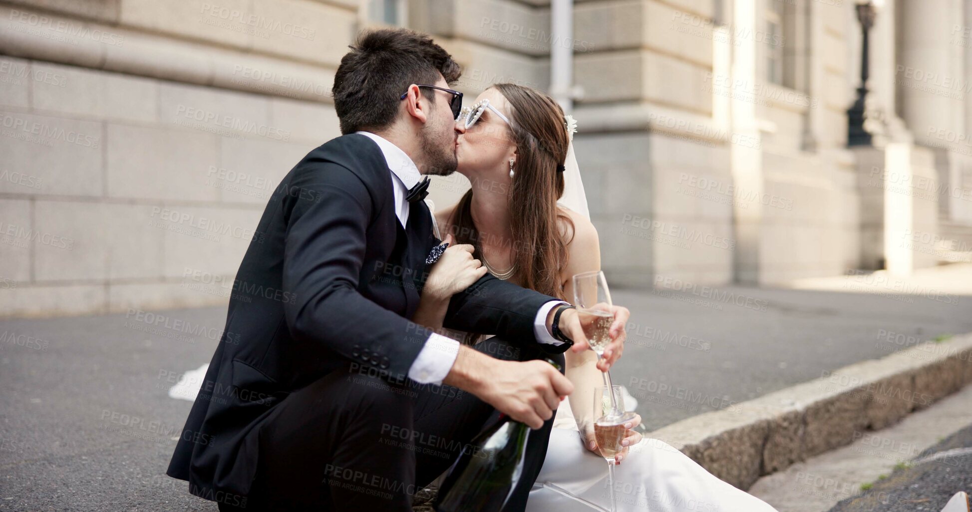 Buy stock photo Wedding, kiss and couple in city with alcohol for ceremony, celebration or commitment with embrace. Romance, love and man and woman in town with champagne for promise, affection and marriage at court