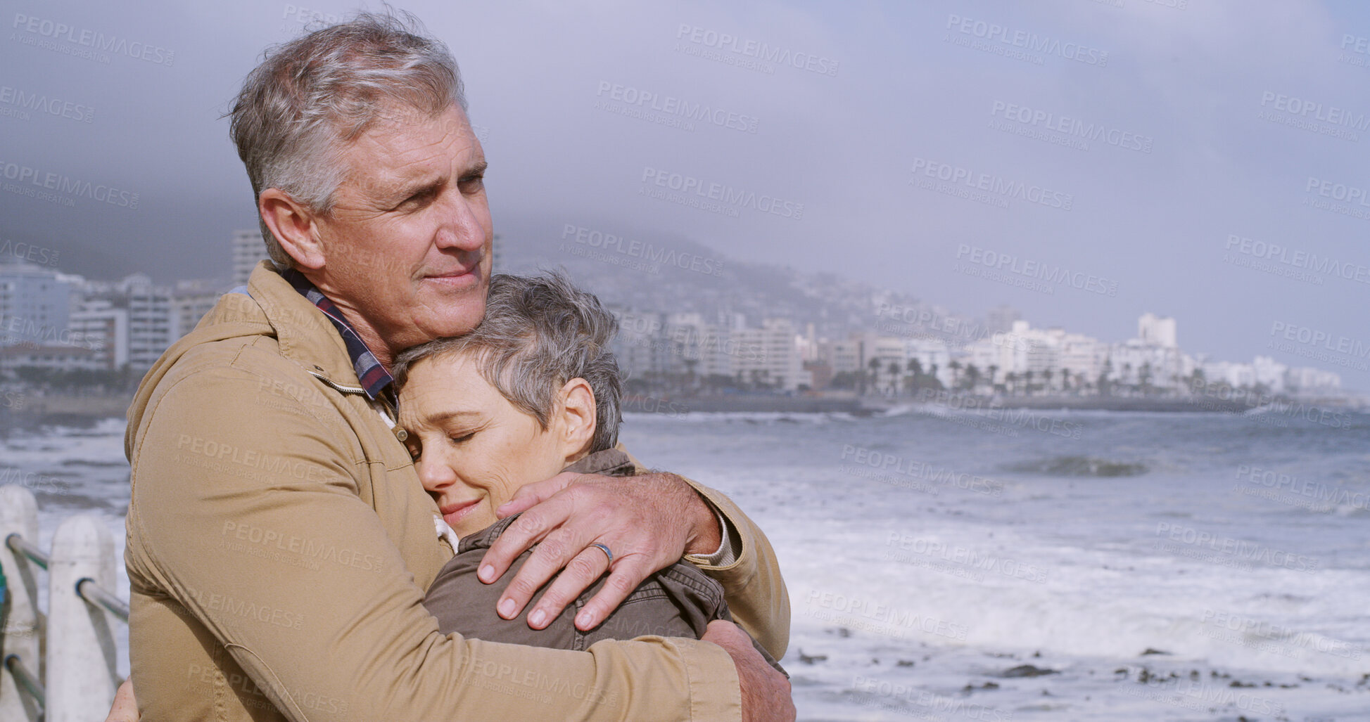 Buy stock photo Mature couple, hug and support by ocean, water and beach for love, partnership and bonding together. Woman, man and embrace in relationship, marriage or care with outdoor, vacation or winter in city