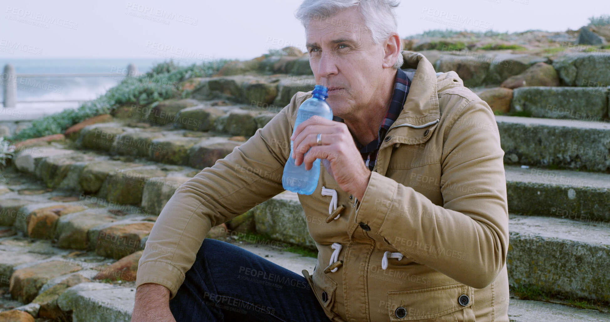 Buy stock photo Senior, man and drinking with water on stairs by beach for hydration, thirst or natural sustainability. Mature, male person or relax with mineral liquid, beverage or refreshment on steps by ocean