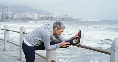 Buy stock photo Mature woman, stretching legs and fitness at ocean with peace, flexibility or running preparation. Retired athlete, warm up or muscle tension relief at seaside for exercise, wellness or care in Italy