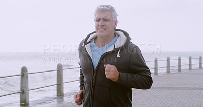 Buy stock photo Senior, man and running with earphones on beach for workout, outdoor exercise or cardio training. Mature, male person or runner with smile by ocean coast for physical activity or fitness in nature