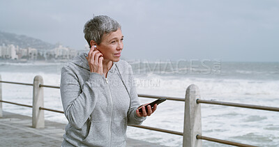 Buy stock photo Mature woman, phone and earphones on promenade with music, reading and workout in morning. Person, smartphone and listening on mobile app with running, streaming and subscription by ocean in Italy