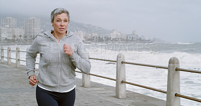 Buy stock photo Running, music and energy with old woman at beach for fitness podcast, wellness and streaming. Athlete, training and workout with senior person and earphones for challenge, exercise and cardio