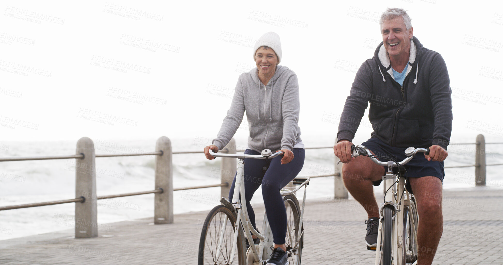 Buy stock photo Senior couple, bicycle and happy on promenade, beach and outdoor in morning with exercise in summer. Man, woman and cycling with smile by sea, ocean and journey for workout with bonding in England 