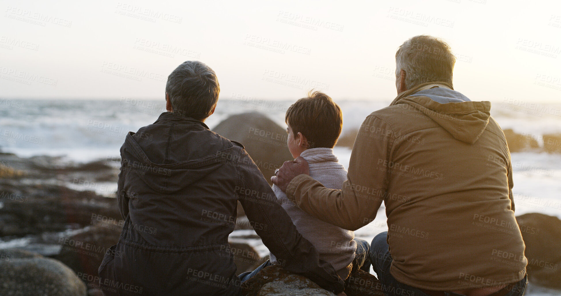 Buy stock photo Family, outdoor and child by sea with grandparents, sunrise and care in morning and nature on holiday. Vacation, back and beach with idea, calm and rock by waves with travel and thinking with bonding