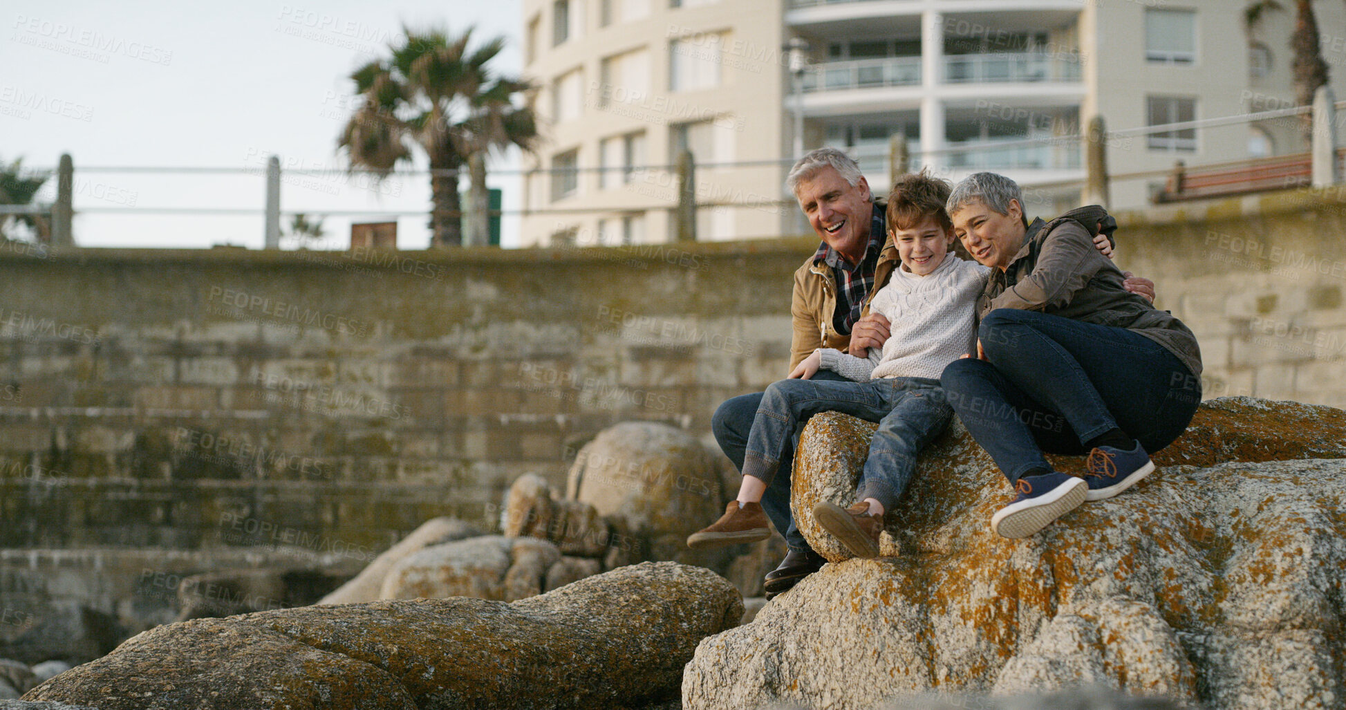 Buy stock photo Grandparents, grandchild and relax on rocks at ocean for family holiday, happy memory and travel adventure. Senior people, boy child and playing together for connection, bonding or trust by coastline