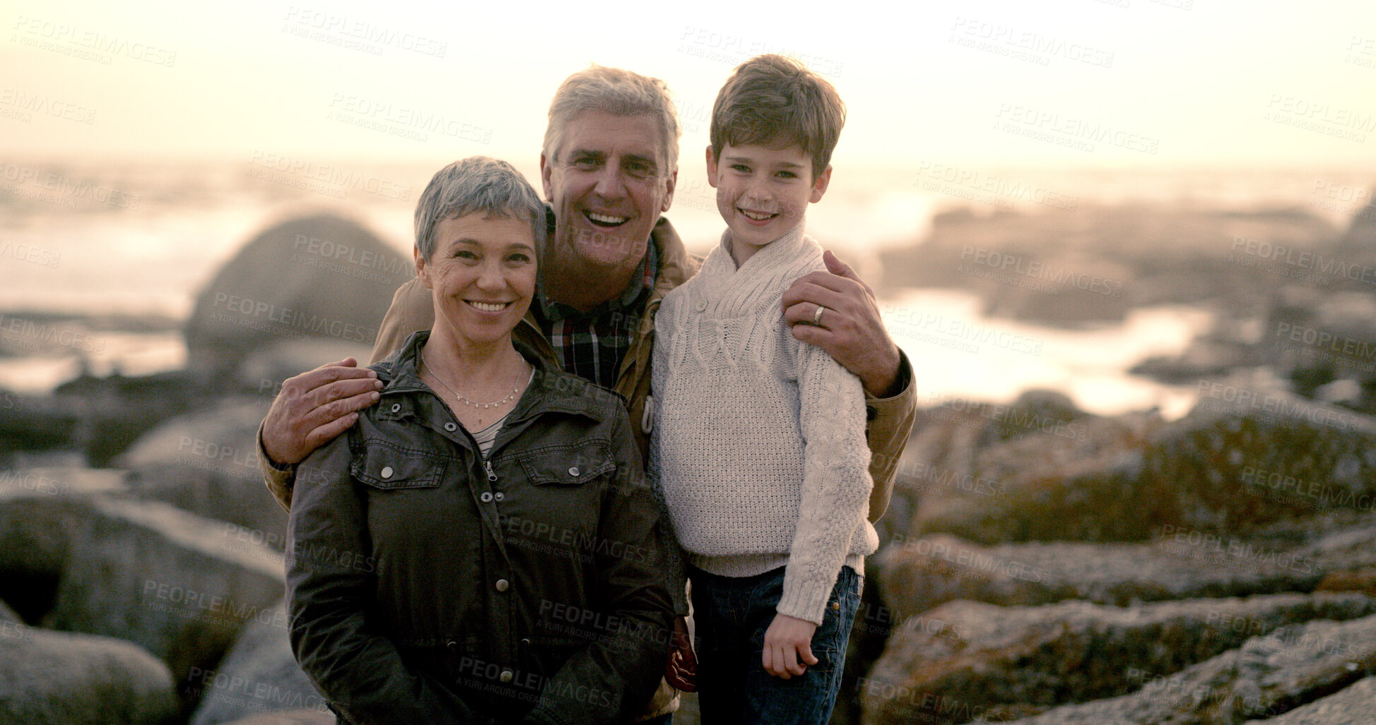 Buy stock photo Happy, sea and portrait of grandparents with child for bonding, fun weekend and relax together at beach. Rocks, family and young boy, grandpa and grandma on holiday, adventure or vacation at sunrise