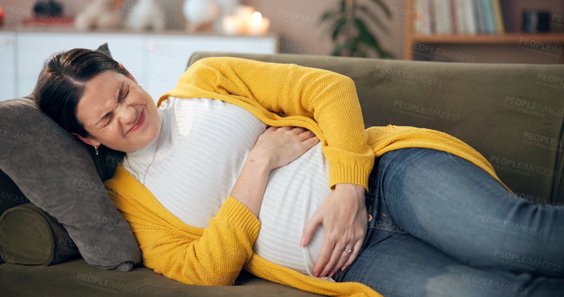 Buy stock photo Pregnant, woman or stress in home with pain, cramping or hold stomach for relief on sofa. Future mom, rest or discomfort in living room for contractions, bloating or prenatal care with worry for baby