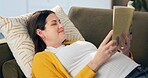 Pregnant woman, book and reading on sofa in home with thinking, smile and relax in living room. Person, mother and literature with story, happy and prenatal growth for belly in lounge at apartment