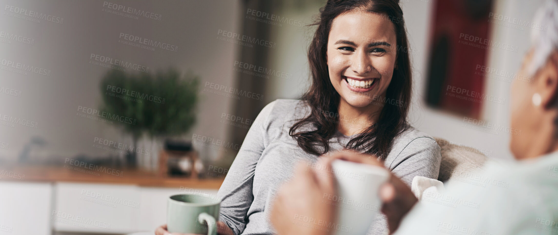 Buy stock photo Shot of a young woman and her mother catching up on the sofa while drinking coffee