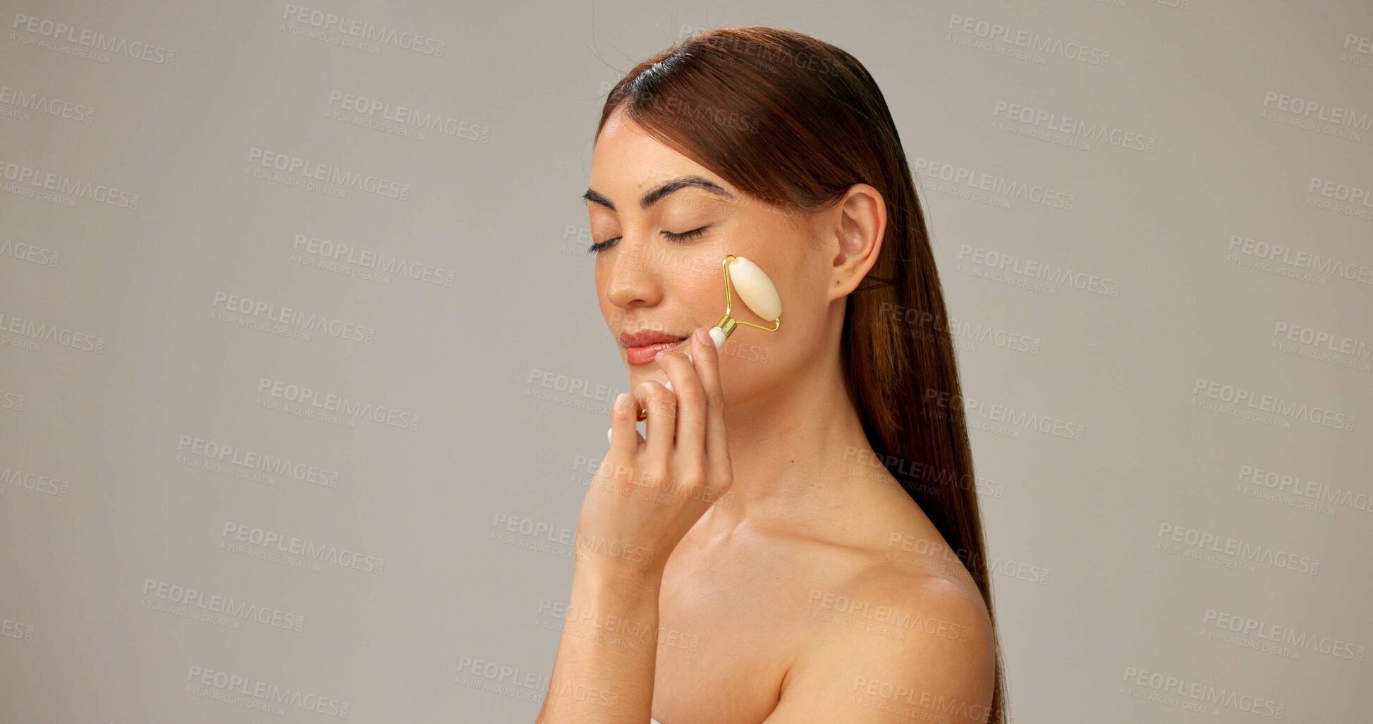 Buy stock photo Happy, face roller and woman with cosmetics skincare and dermatology on gray studio background. Person, model and girl with treatment, grooming routine and aesthetic with healthy skin and rose quartz