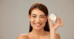 Portrait, smile and woman with cream, skincare and dermatology on gray studio background. Person, model and girl with happiness, cosmetics and container for creme, healthy skin and grooming routine