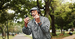 Headphones, senior man and smartphone with celebration in park for good news, giveaway winner and gambling bonus. Old person, phone and excited in nature for lottery prize or competition notification