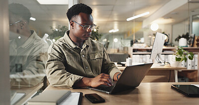 Buy stock photo Black man, laptop and typing at night in office for project, review or deadline at media company. African person, writer and computer for feedback, overtime and editing article at creative agency