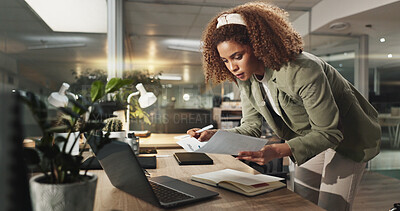 Buy stock photo Woman, laptop and documents at night in office for project, review or deadline at media company. African person, writer and computer for feedback, overtime or paperwork for article at creative agency