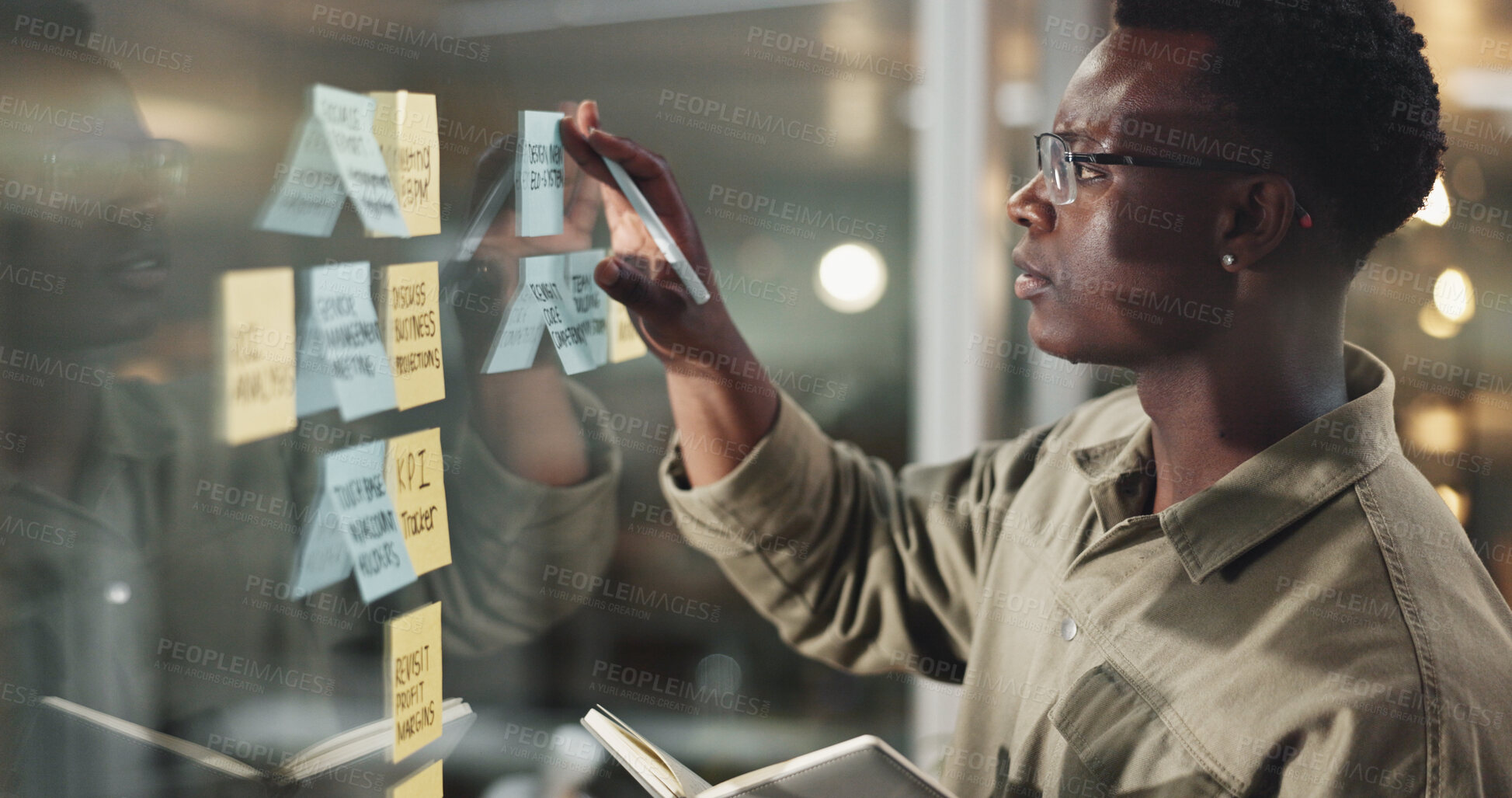 Buy stock photo Business, man and planning with sticky notes on glass wall for problem solving, notebook or project management. Night, black person and designer at creative agency with calendar deadline and schedule