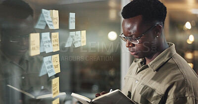 Buy stock photo Business, black man and serious with writing in notebook by glass wall for problem solving or project management. Sticky notes, night and designer at creative agency with planning ideas and strategy