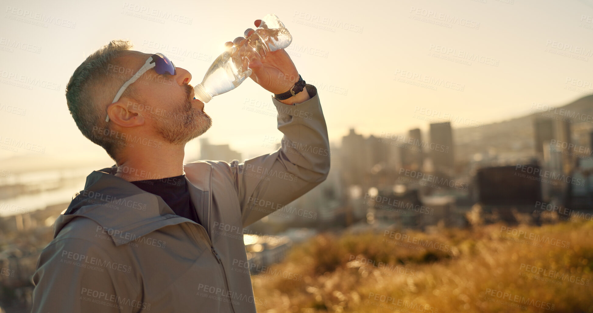 Buy stock photo City, nature and man drinking water for fitness, health or wellness with morning exercise on hill. Relax, athlete and runner on mountain with bottle, break and hydration on outdoor workout at sunrise