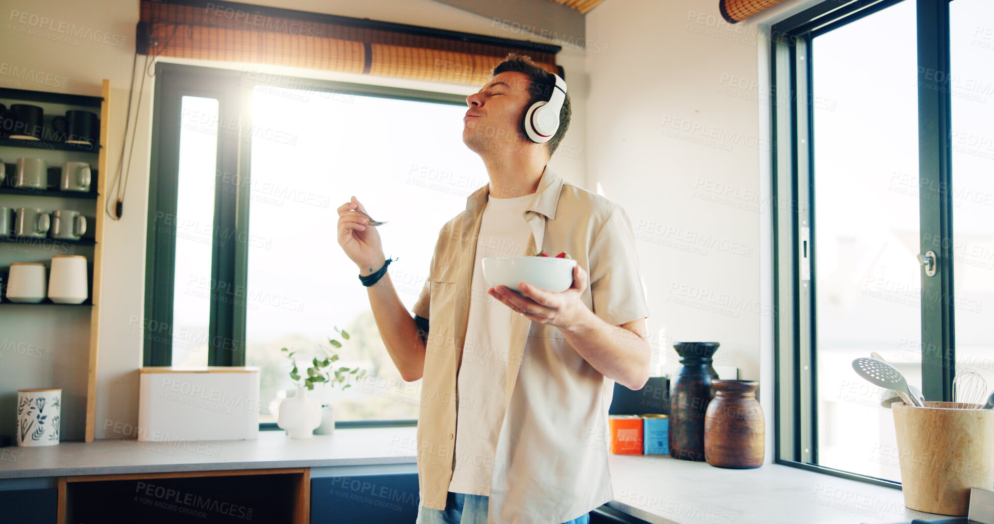 Buy stock photo Headphones, eating and man with fruit salad in kitchen  listening to podcast in morning for self care. Audio tech, health and male person enjoying breakfast for diet, nutrition or wellness in home.