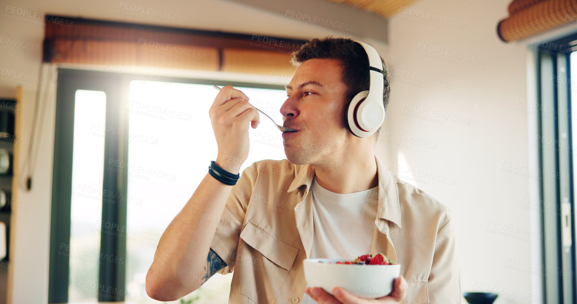 Buy stock photo Headphones, eating and man with breakfast in kitchen  listening to podcast in morning for self care. Audio tech, health and male person enjoying fruit salad for diet, nutrition or wellness in home.