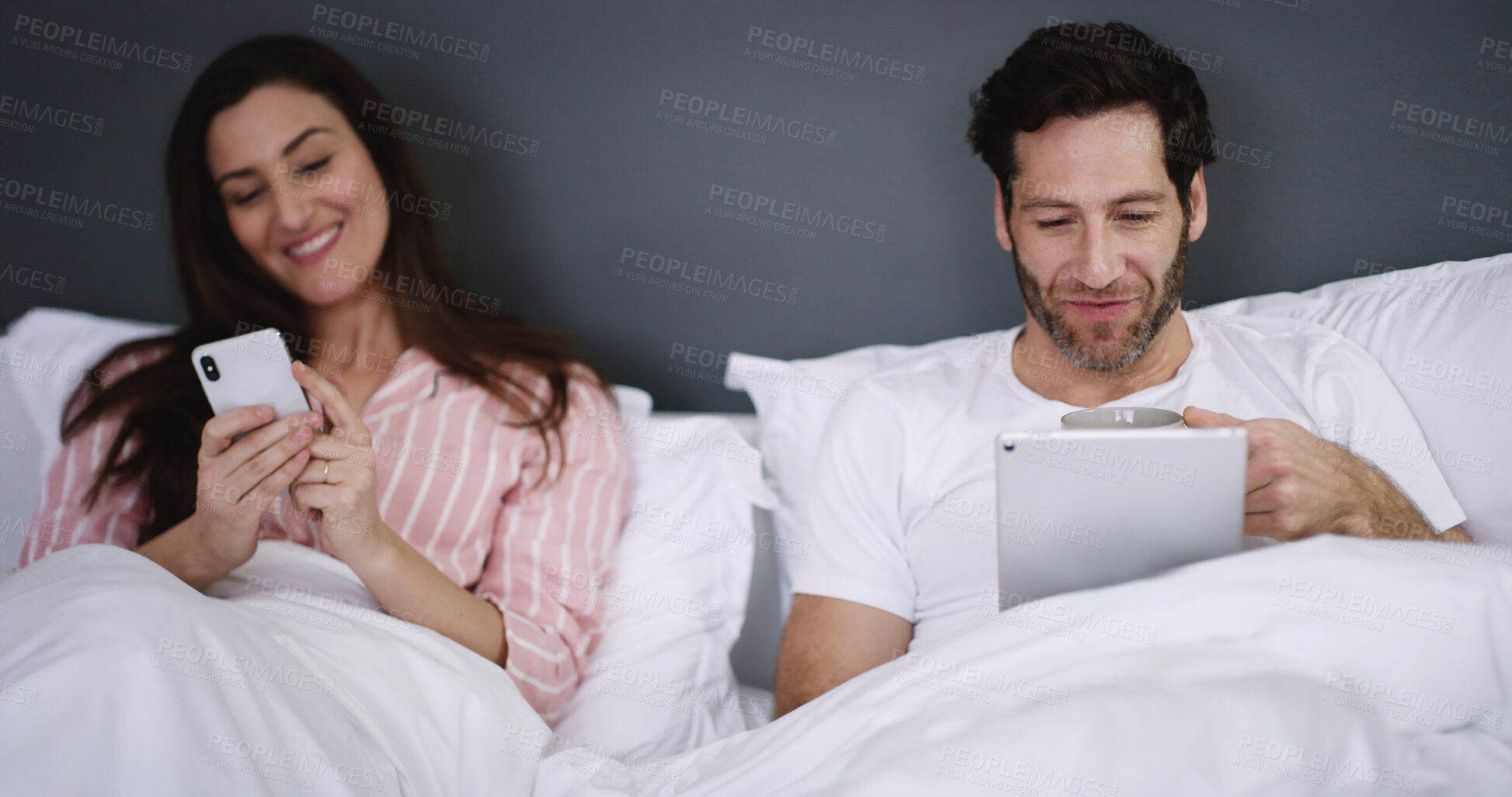 Buy stock photo Phone, tablet and couple resting in bed in home for networking, connectivity or browsing online. Happy, relax and young people with cellphone and digital technology in bedroom for contact in house.