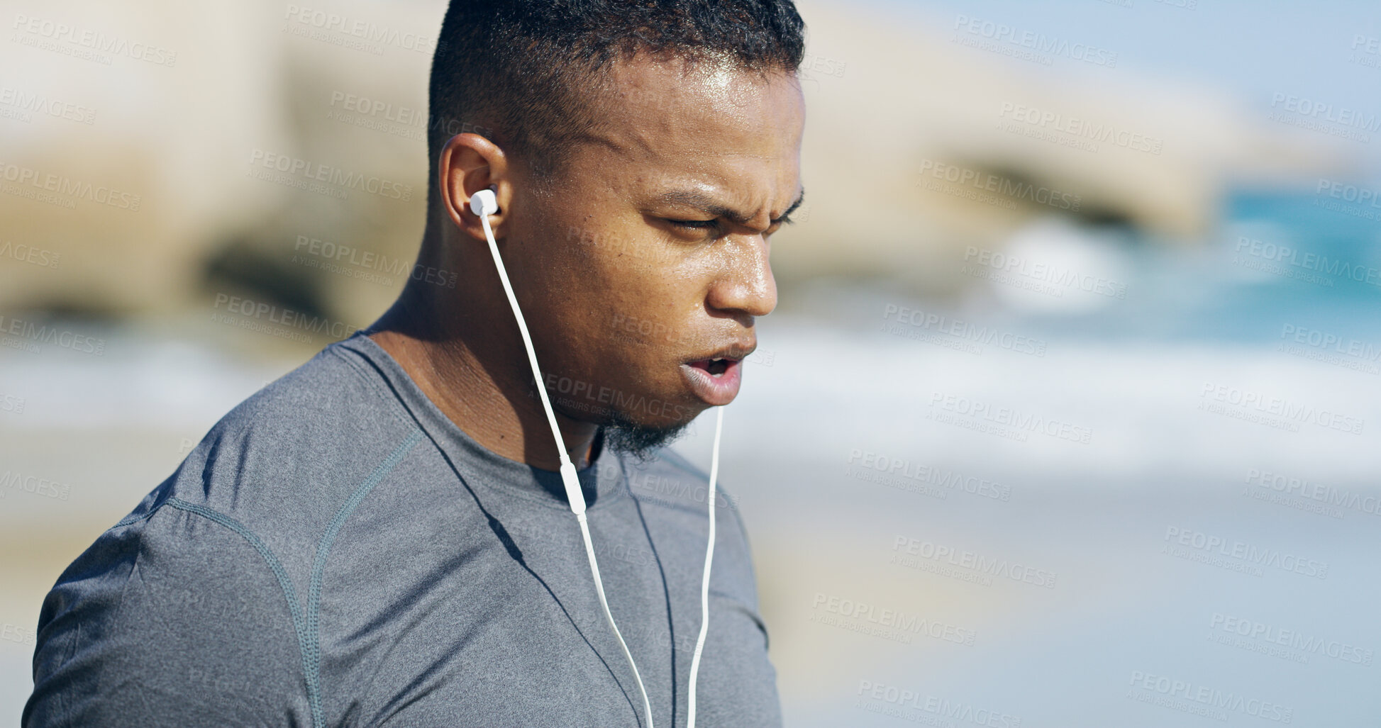 Buy stock photo Beach, man and tired with breathing for fitness, exercise and sprinter with workout music for wellness outdoor. Ocean, male person and runner with sweat for training, cardio and earphones for podcast