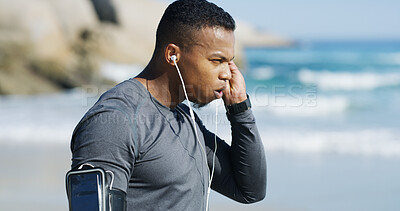 Buy stock photo Fitness, man and tired with earphones on beach, exercise and sprinter with workout music for wellness outdoor. Ocean, male person and runner with breathing for training, cardio and rest with podcast