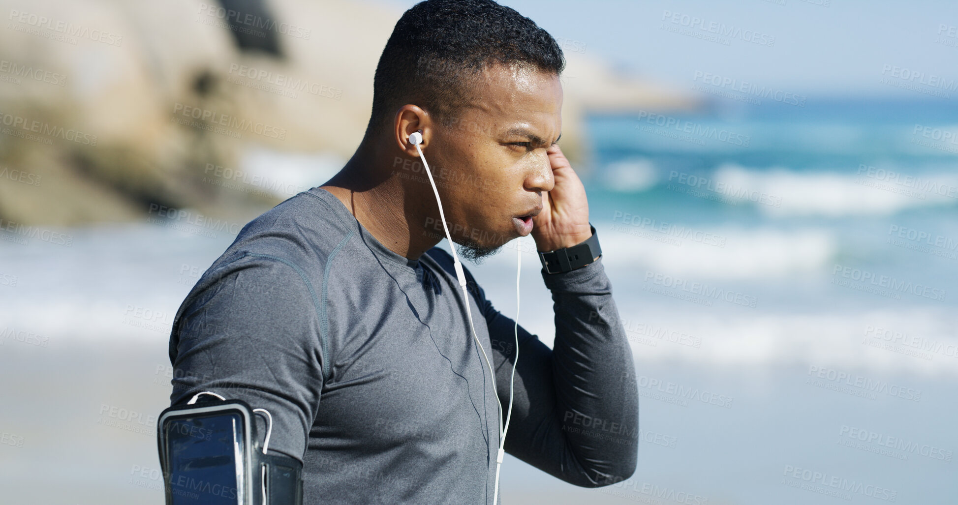 Buy stock photo Fitness, man and tired with earphones on beach, exercise and sprinter with workout music for wellness outdoor. Ocean, male person and runner with breathing for training, cardio and rest with podcast