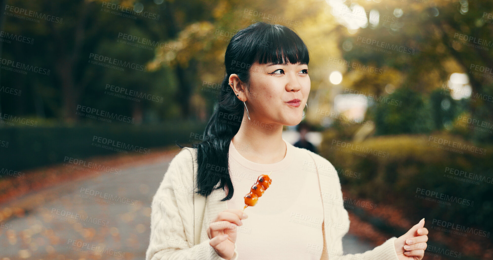 Buy stock photo Japanese woman, walking and eating street food in park for traditional dessert, sightseeing and cultural cuisine. Tourist, hungry person and happy with dango dumpling, skewer snack and exploring city