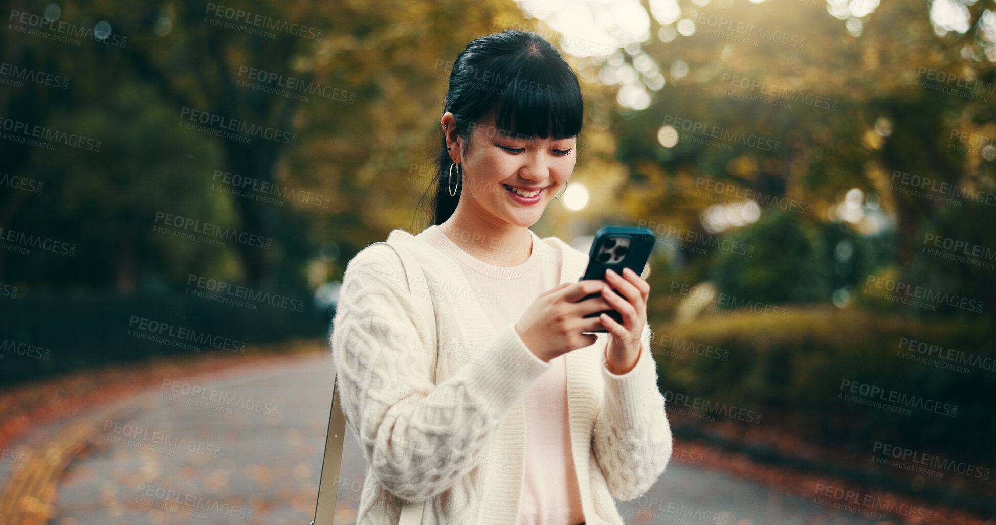 Buy stock photo Japanese woman, walking and smartphone in park for online networking, dating app and text message response. Person, phone and smile for social media post, notification and browsing internet in street