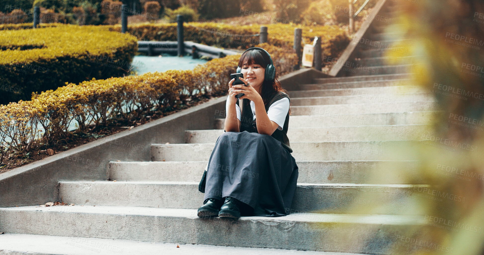 Buy stock photo Phone, headphones and girl on stairs in park with smile, search and and online connection. Relax, smartphone and happy Japanese woman on steps in outdoor garden with mobile app for music streaming