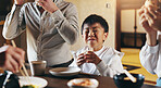 Japanese boy, child and eating with family, happy or together with bonding, diet or nutrition in home. Kid, people and food at dinner for meal, care and smile with parents, excited or hungry in house