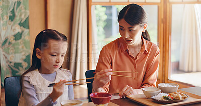 Buy stock photo Mom, girl and chopsticks at lunch, home or teaching for food, eating or bonding for love in dining room. People, mother and daughter family house for meal, diet or nutrition with learning in Japan