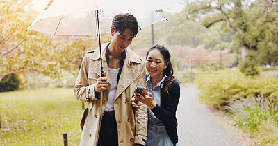 Buy stock photo Umbrella, man and woman in park with phone, checking schedule or online map on morning date. Smartphone, scroll or Japanese couple with mobile app on romantic walk in garden with cover in winter rain