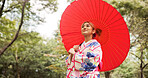 Park, umbrella and happy woman with fashion, thinking and travel with smile in woods. Street, kimono and parasol with walking, outdoor and journey with style and traditional Japanese dress in nature