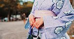 Fashion, hands and woman in kimono in city for traditional Japanese style, cultural elegance and heritage with bag. Floral pattern, fabric or person in yukata outdoor for indigenous outfit or closeup