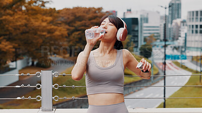 Buy stock photo Drinking water, outdoor and woman with fitness, headphones and wellness with workout. Japanese person, runner and athlete in city, hydration and listening to music, sound and thirsty with rest