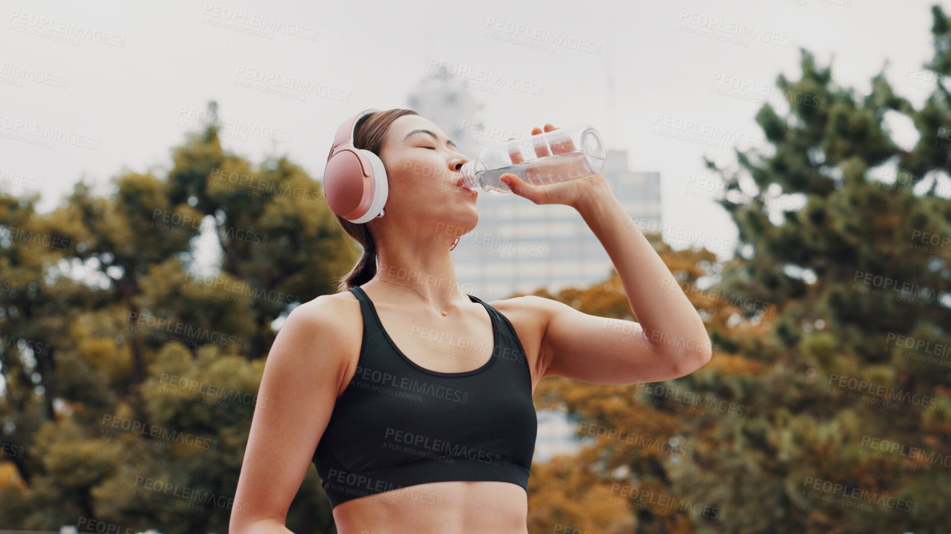 Buy stock photo Drinking water, outdoor and woman with fitness, healthy and wellness with workout. Japanese person, runner and athlete in city, headphones and listening to music, sound and thirsty with hydration