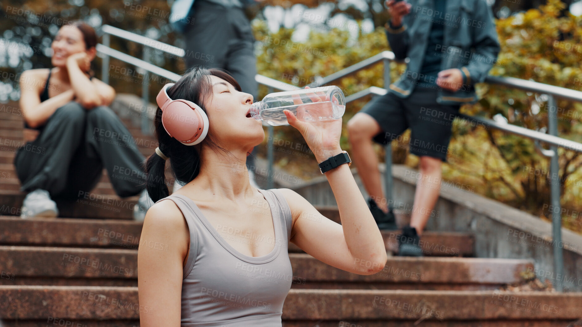 Buy stock photo Woman, headphones and drinking water for exercise in park, mineral liquid and fitness recovery. Female person, athlete and nutrition for hydration on stairs, workout break and streaming song in Japan