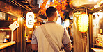 Night, street market and back of man in Japan city on vacation for shopping, travel destination and festival. Culture, traditional holiday and walking with person for urban, tourism or heritage