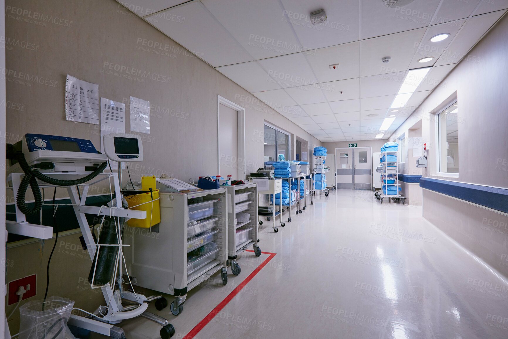 Buy stock photo Shot of an empty passage way with medical equipment alongside the walls at a hospital