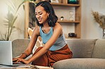 .Smiling mixed race woman browsing internet on a laptop at home. One happy hispanic entrepreneur sitting alone on her sofa and blogging over a weekend. Relaxing in a living room and typing a blog post