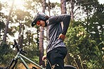 Bicycle, back pain injury and man in forest cycling for fitness, outdoor travel or sports wellness with nature lens flare. Marathon sport person training in mountain bike or motorcycle muscle injury