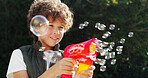 Smile, child and toy with bubbles outdoor for playful fun, learning activity and sensory stimulation. Boy, gun and soap with childhood games, fine motor skills and creative imagination in backyard