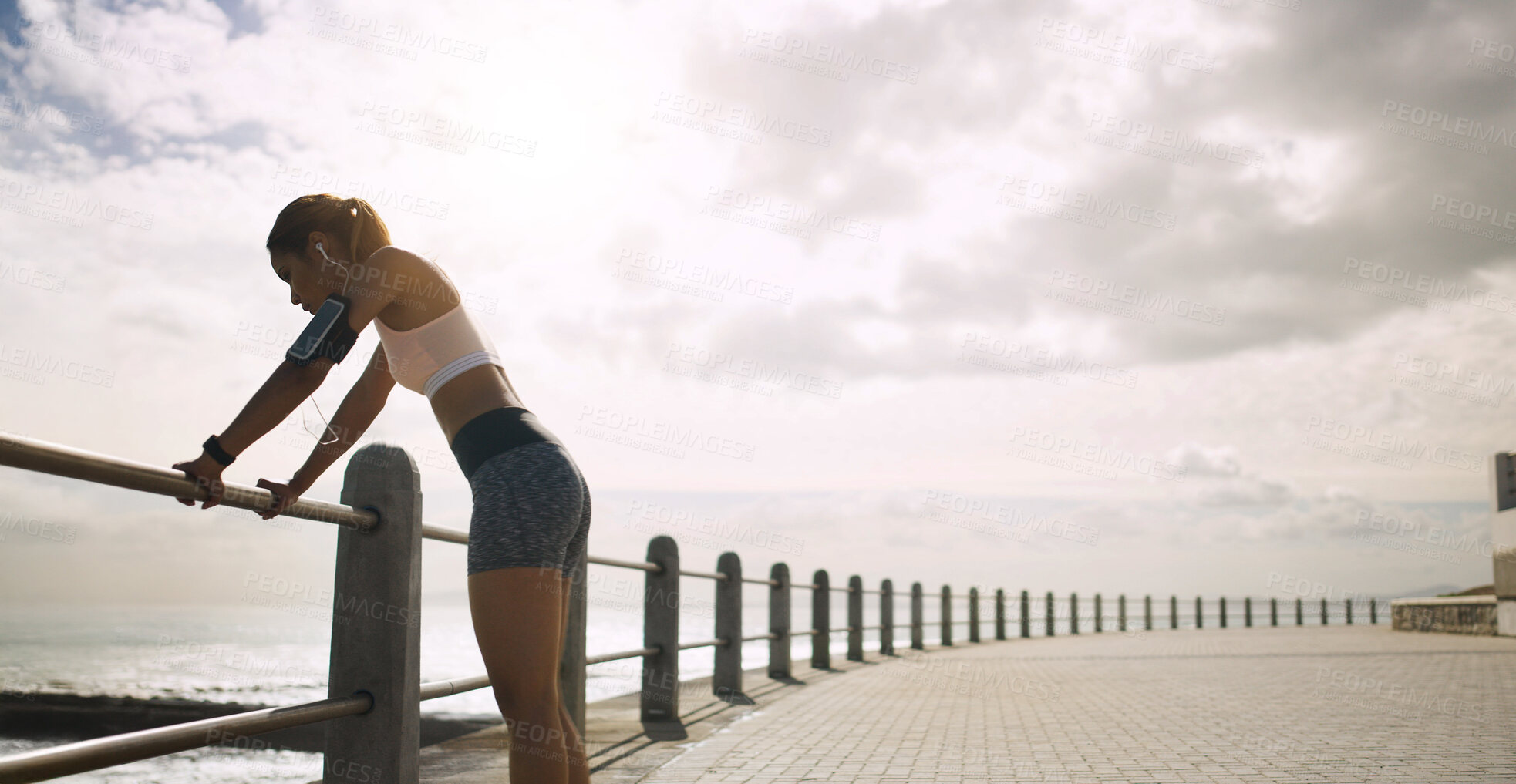 Buy stock photo Seaside, woman and retired from running with fitness on earphones for wellness, health and self care. Female person, cloudy sky and space on break with jogging as workout, training and exercise