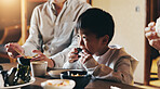 Japanese boy, family and eating in home with feeding, smile and noodles together with sushi. Food, hungry and dinner table with love, kid and care with chopsticks and meal for health and nutrition