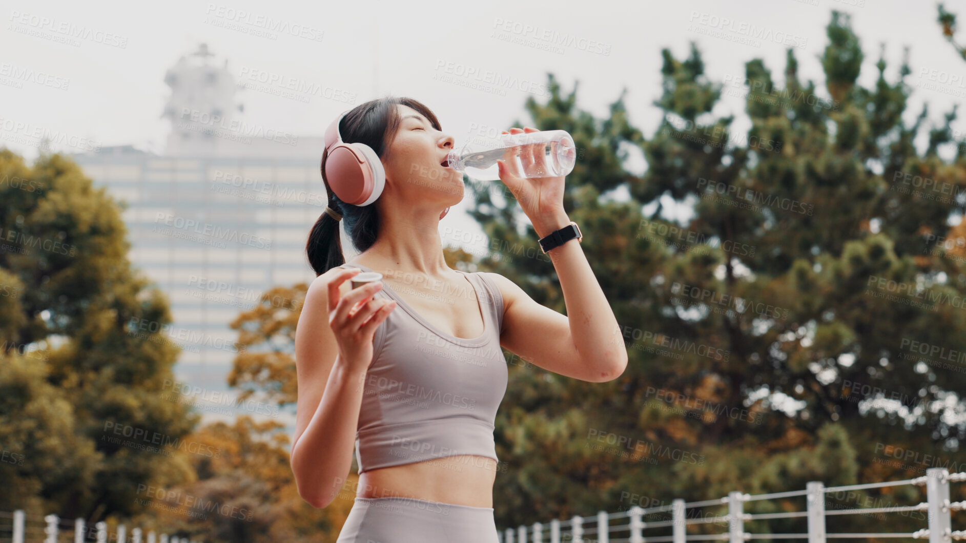 Buy stock photo Drinking water, outdoor and woman with fitness, wellness and rest with workout. Japanese person, runner and athlete in city, headphones and listening to music, healthy and thirsty with hydration