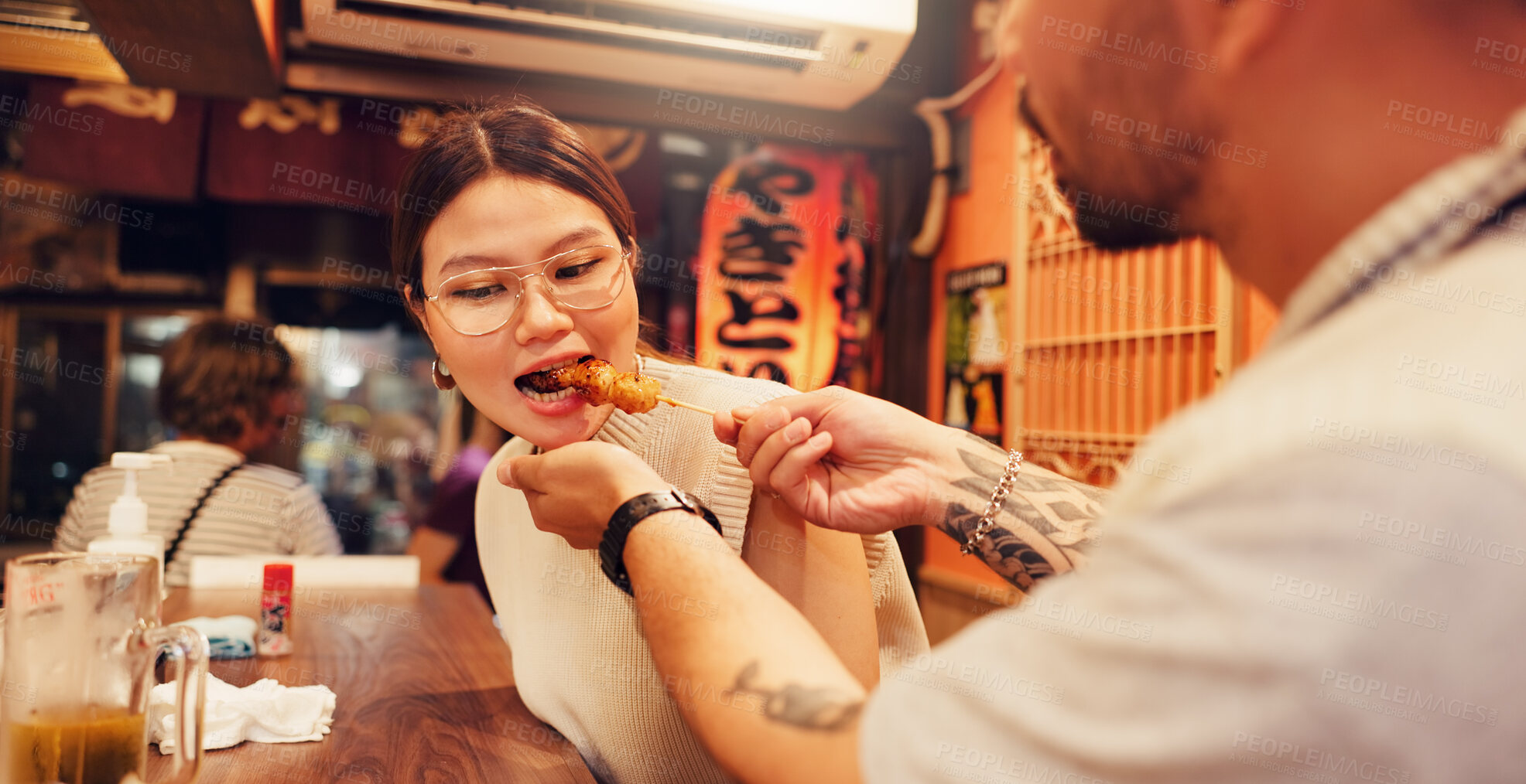 Buy stock photo Japanese man, woman and feeding with Asian food in city for romantic dinner, meal or nutrition. Couple, eating and bonding together with cuisine, culture or recipe for sharing or night in restaurant